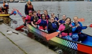 A group of young adults and children, dressed in colorful, pink and blue counters, counter full of green yellow widen boat float, just off the dock with the paddles