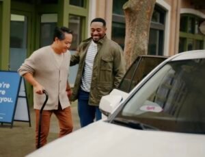 Lift driver is assisting a gentleman with a cane into the pasture door of his white car