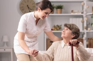 Elderly female client with cane is being helped by female aide