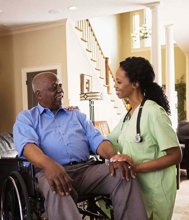 Man in wheelchair being tended to by female aide in home
