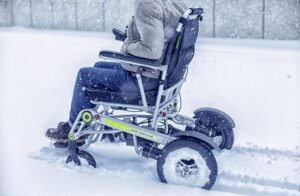 A wheelchair user stuck in snow while on wheelchair while dressed appropriately for the weather.